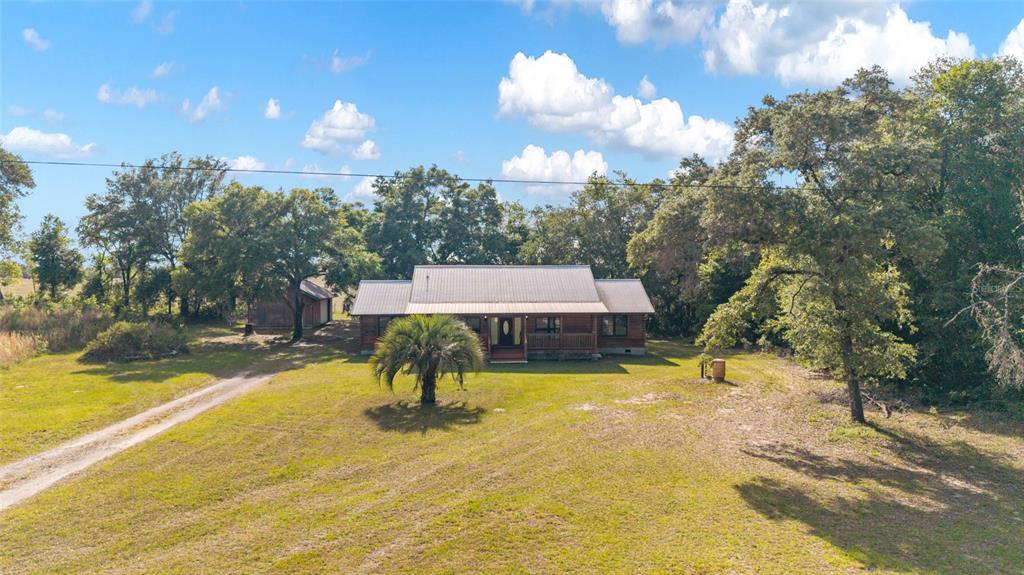 A wooden house with a metal roof sits on a grassy lot with mature trees — 1230 SW VALENCIA HEIGHTS AVENUE, DUNNELLON, FL