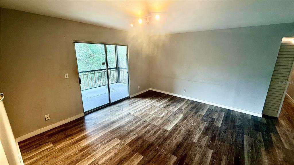 An empty room features gray walls, wood-look flooring, and a sliding glass door to a balcony — 6519 W NEWBERRY ROAD UNIT 812, GAINESVILLE, FL