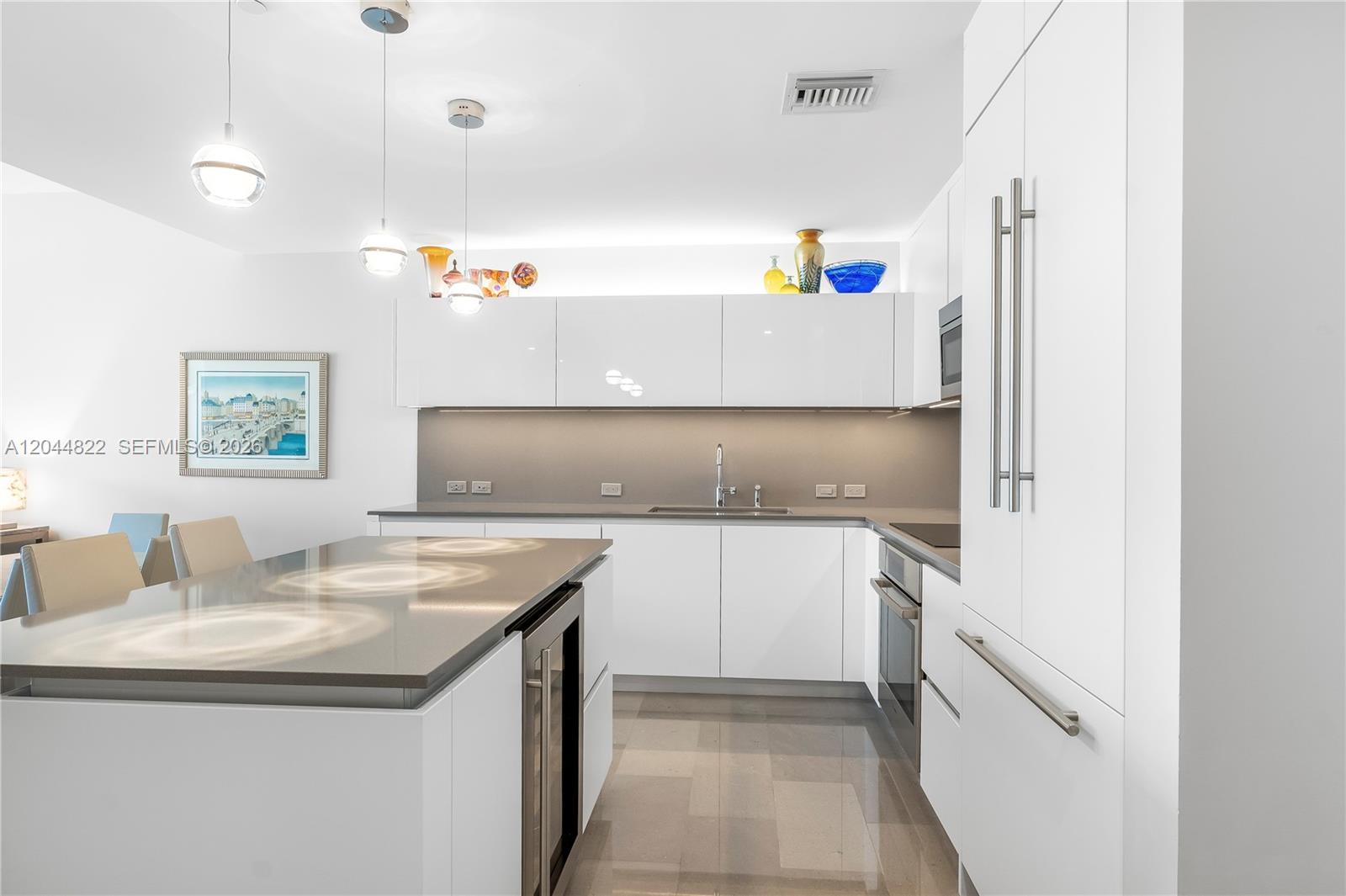 A modern kitchen features white cabinetry, a gray island, and stainless steel appliances — 68 SE 6th St # 810, Miami FL 33131, MIAMI, FL