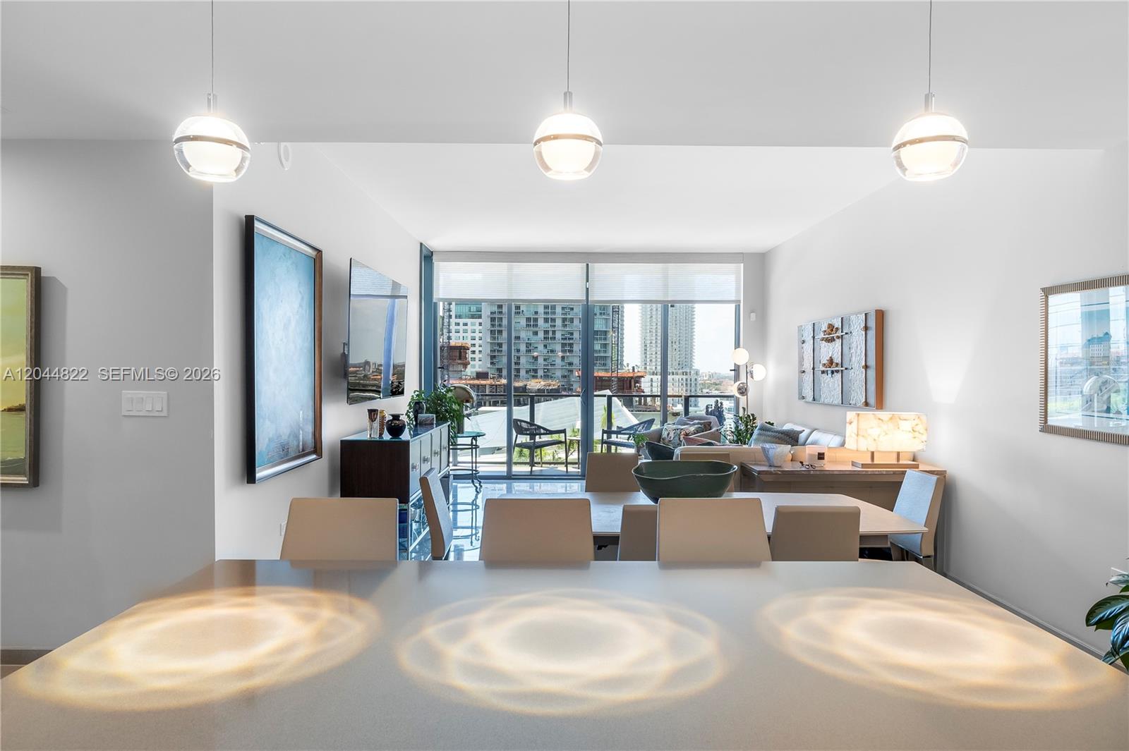 A modern dining and living area features three pendant lights, a balcony, and city views — 68 SE 6th St # 810, Miami FL 33131, MIAMI, FL