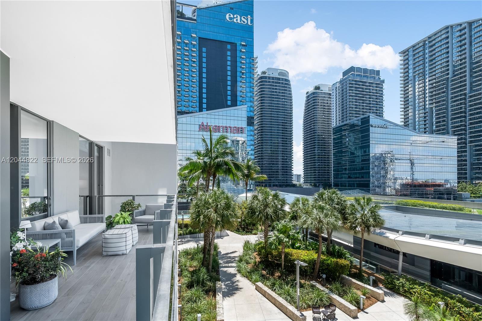 A balcony with outdoor seating overlooks a landscaped courtyard surrounded by modern high-rise buildings — 68 SE 6th St # 810, Miami FL 33131, MIAMI, FL