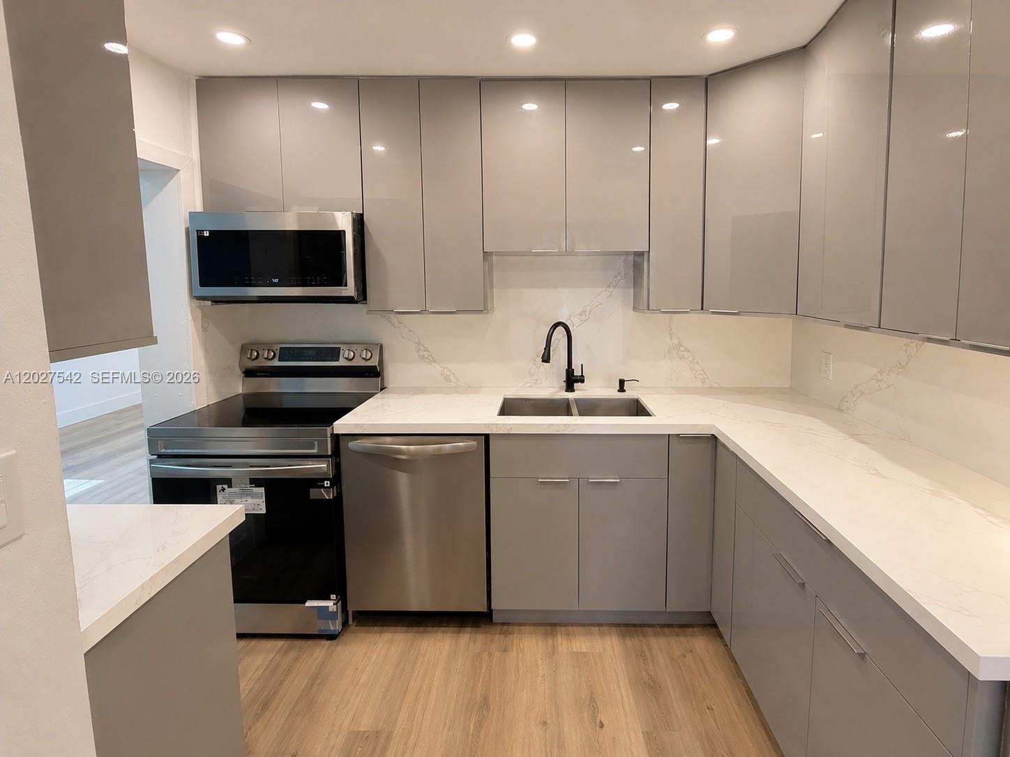 A modern kitchen features gray flat-panel cabinets, stainless steel appliances, and white marble-look countertops — 2627 NE 213th St, Miami FL 33180, MIAMI, FL