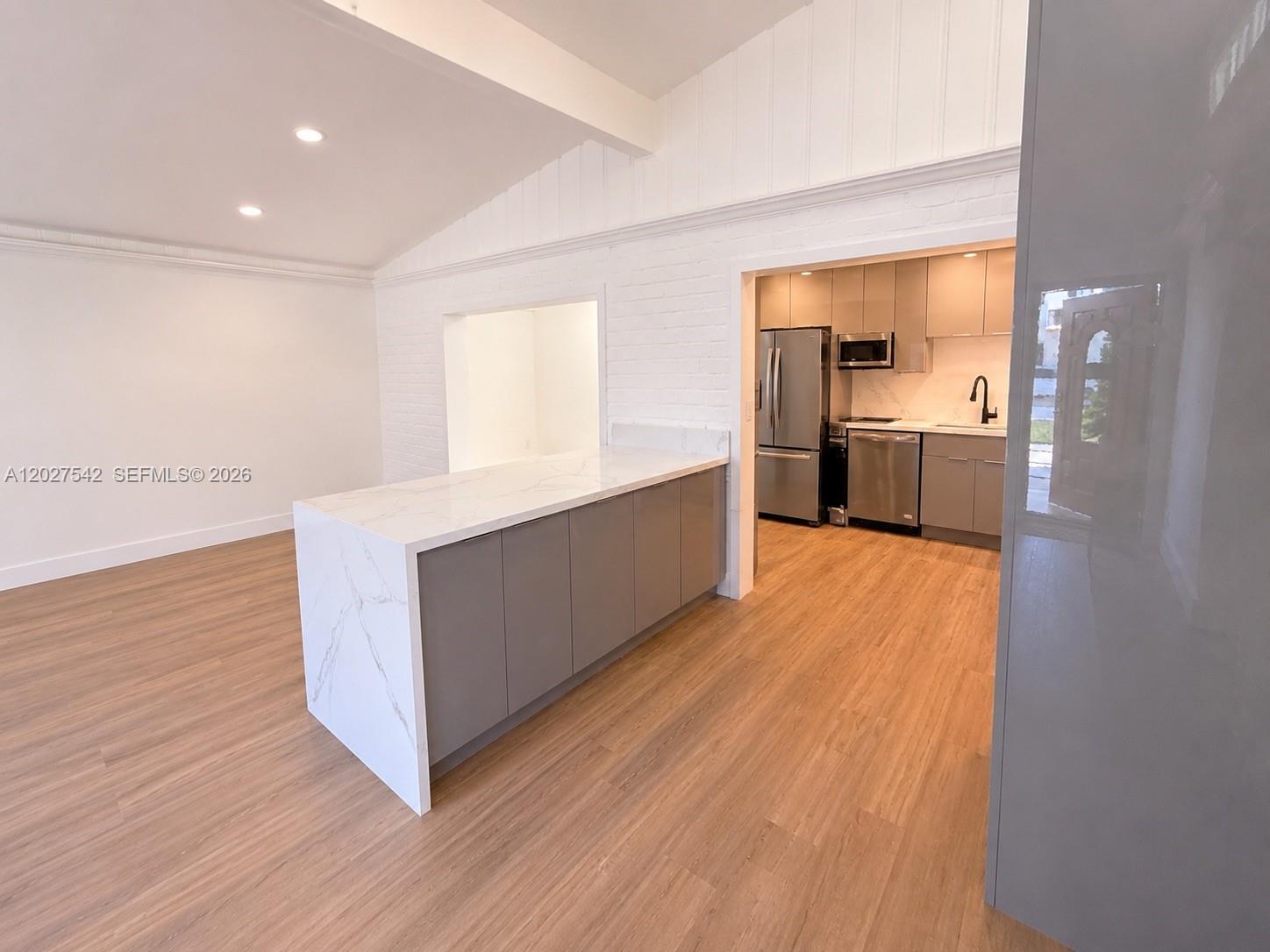 A kitchen features a marble-topped island, gray cabinetry, and light wood flooring — 2627 NE 213th St, Miami FL 33180, MIAMI, FL