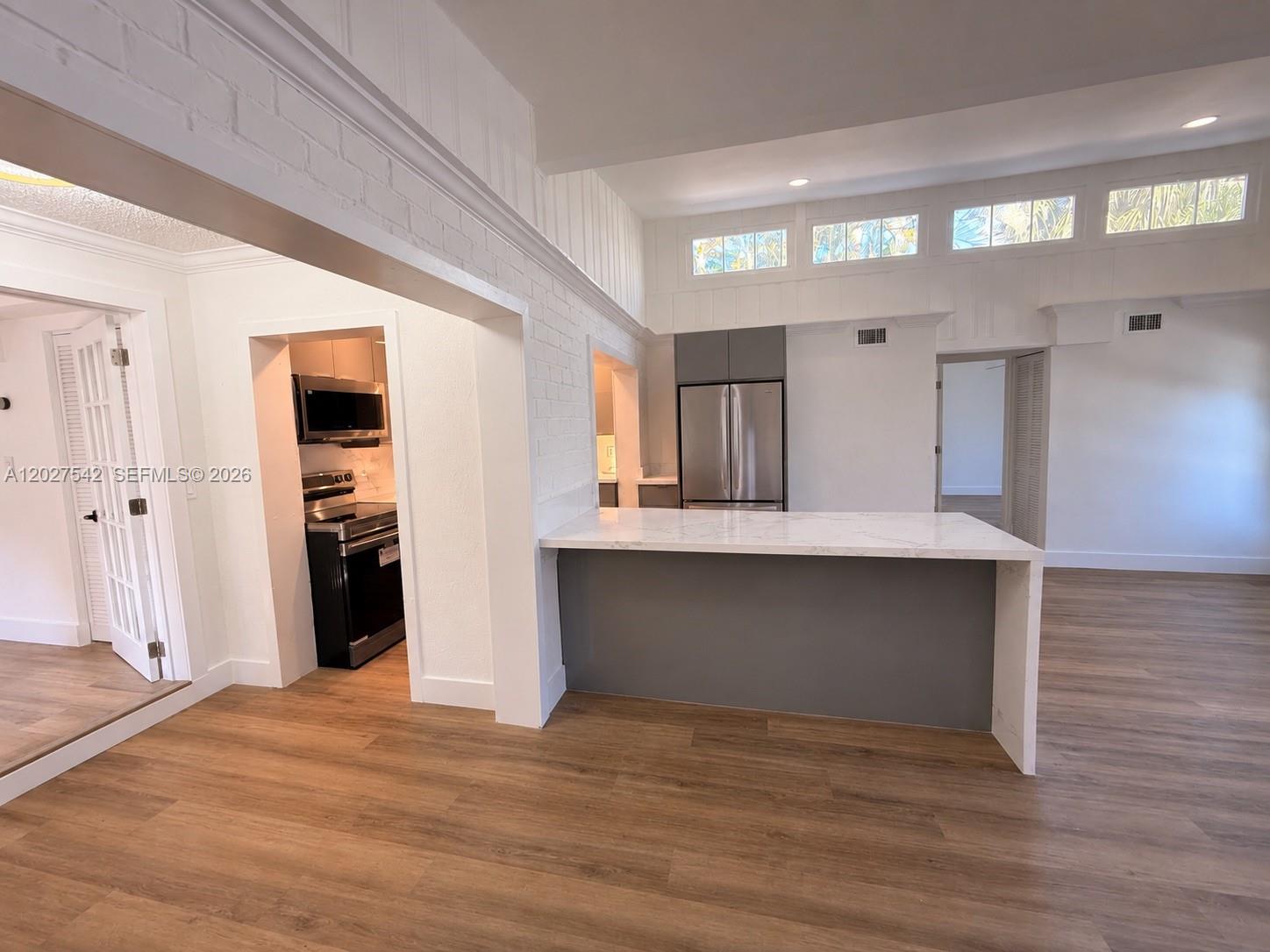 A kitchen features a white marble-topped island, gray cabinetry, and light wood-look flooring — 2627 NE 213th St, Miami FL 33180, MIAMI, FL