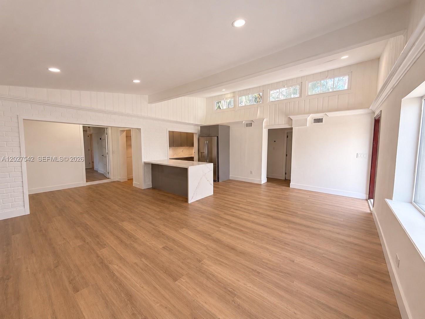 This open-concept living area features light wood flooring, white walls, and a kitchen island — 2627 NE 213th St, Miami FL 33180, MIAMI, FL