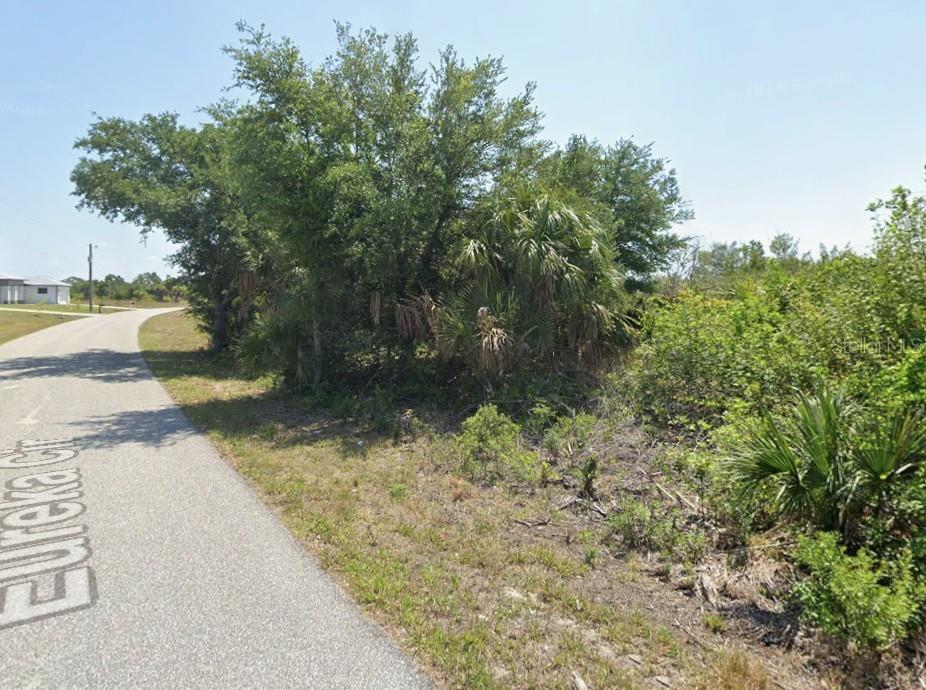 A paved road runs alongside a vacant, wooded lot with trees and low-lying vegetation — 13153 EUREKA CIRCLE, PORT CHARLOTTE, FL