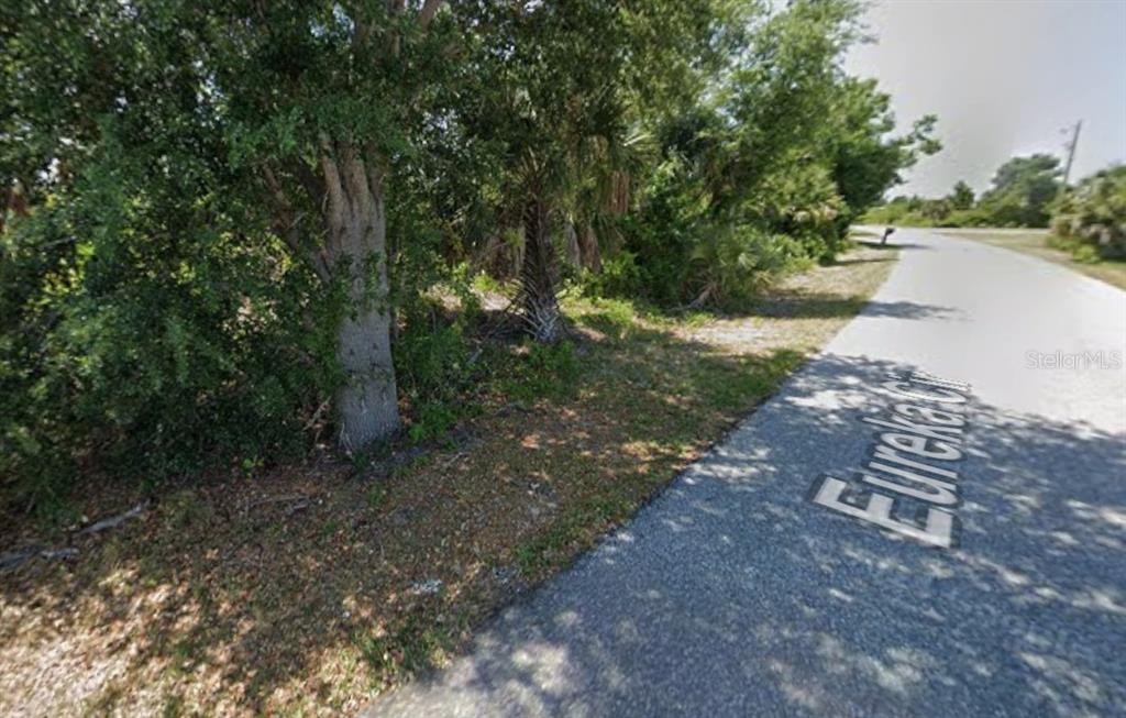 A paved road curves past a wooded lot with trees and dense vegetation — 13153 EUREKA CIRCLE, PORT CHARLOTTE, FL