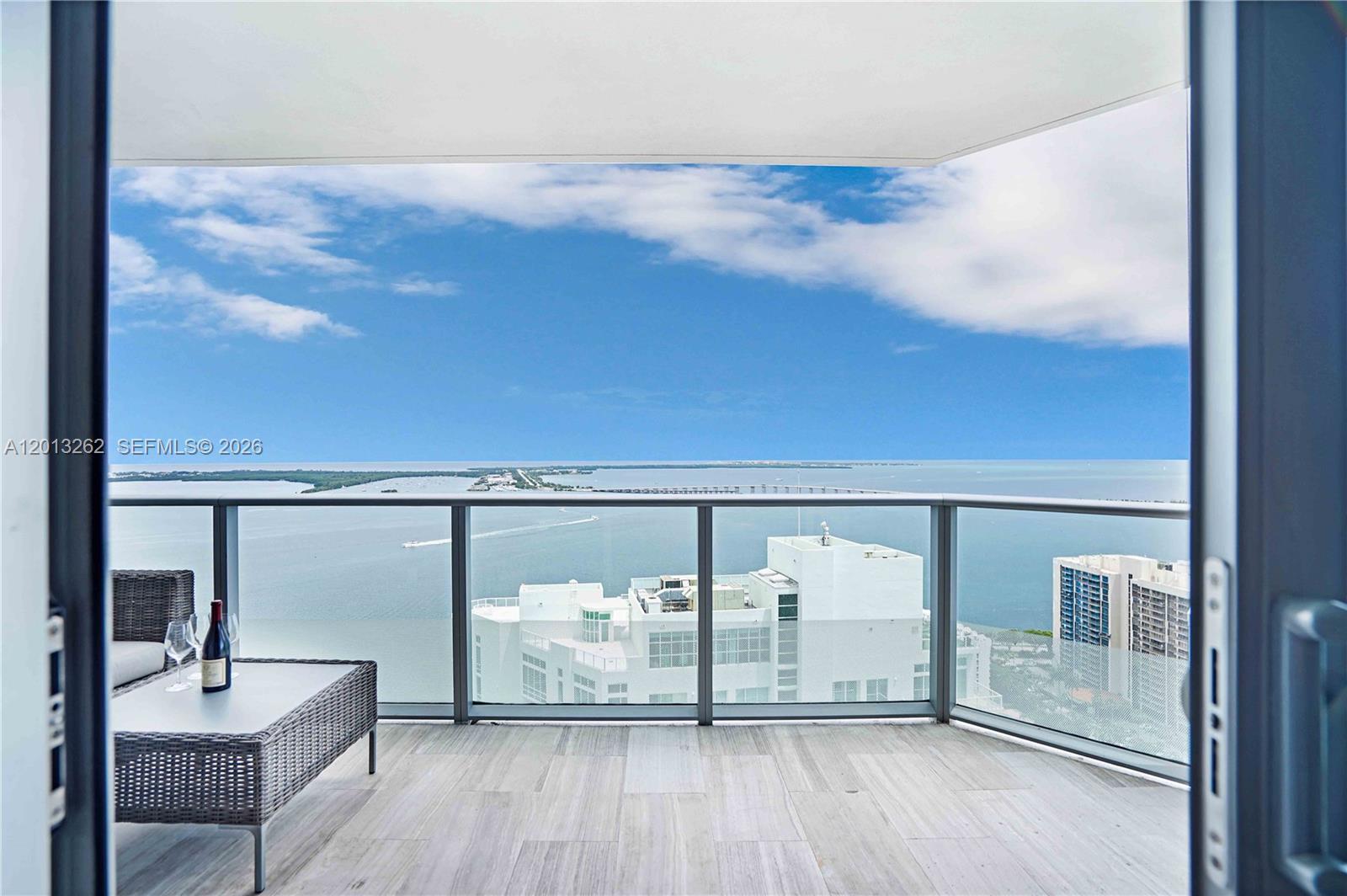 A balcony with light-colored tile flooring overlooks a bay and distant city skyline — 1300 Brickell Bay Dr # 3402, Miami FL 33131, MIAMI, FL