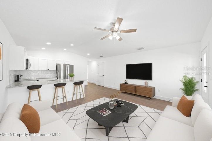 This open-concept living room and kitchen features white cabinetry, stainless appliances, and wood flooring — 15176 GONZO ROAD, BROOKSVILLE, FL