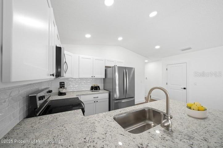 A modern kitchen features white cabinets, granite countertops, stainless steel appliances, and a central island — 15176 GONZO ROAD, BROOKSVILLE, FL