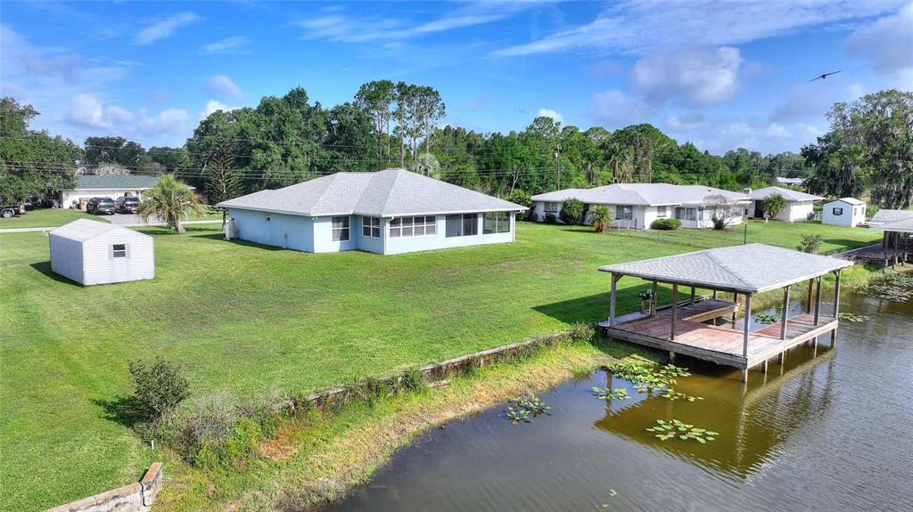 A light blue house with a dock sits on a grassy lot next to water — 6225 AMARYLLIS DRIVE, INDIAN LAKE ESTATES, FL