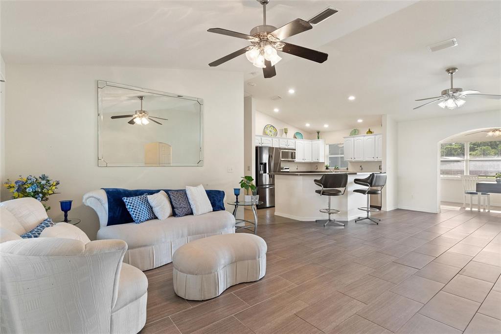 A living room with tile floors and a ceiling fan opens into a white kitchen — 6225 AMARYLLIS DRIVE, INDIAN LAKE ESTATES, FL
