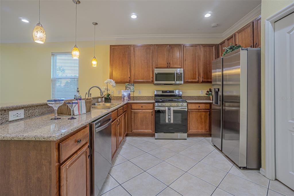 A kitchen features wood cabinets, stainless steel appliances, granite countertops, and tile flooring — 20520 SULTANA COURT, TAMPA, FL