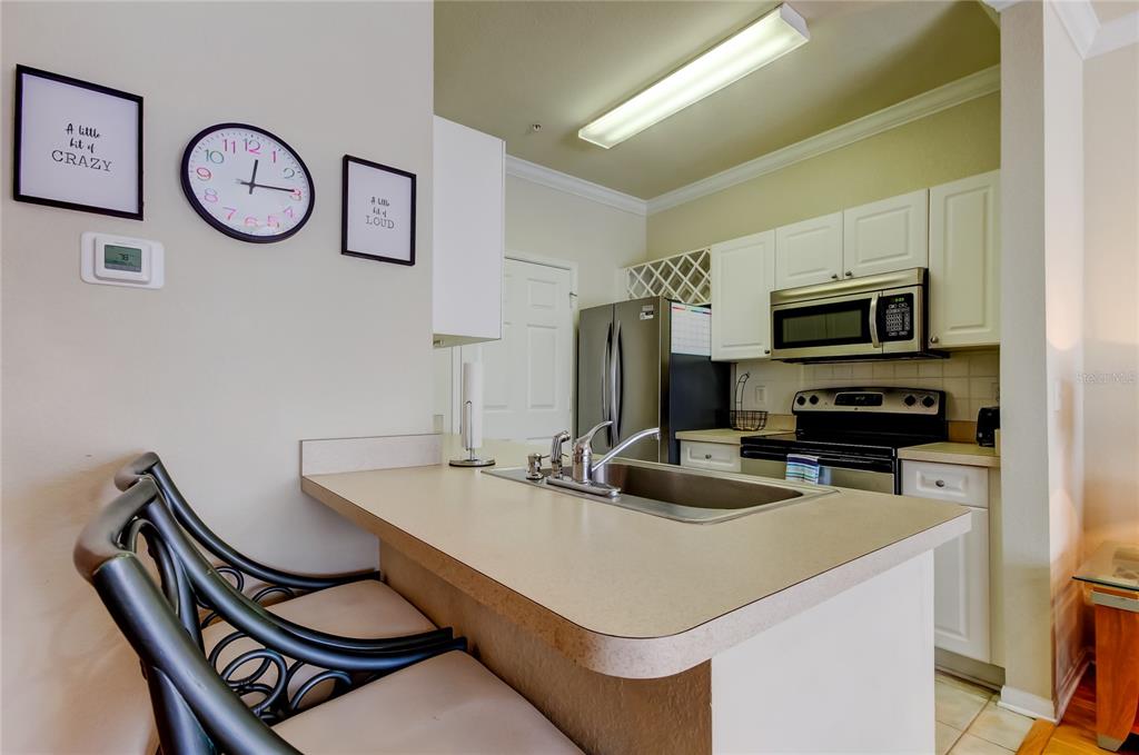A kitchen features a breakfast bar, white cabinets, stainless steel appliances, and a double sink — 1216 S MISSOURI AVENUE UNIT 220, CLEARWATER, FL