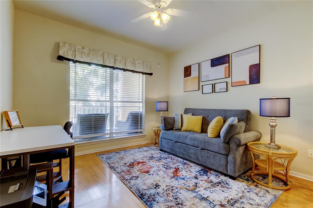 A living room features a gray sofa, a patterned rug, a desk, and a window — 1216 S MISSOURI AVENUE UNIT 220, CLEARWATER, FL