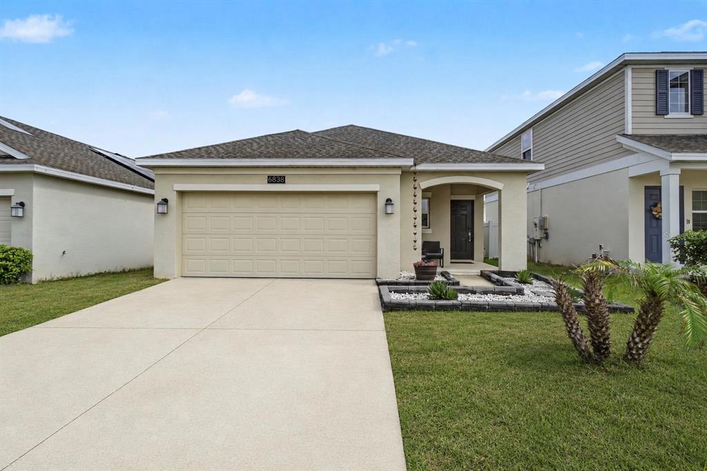 A single-story house with a beige stucco exterior, a two-car garage, and a small front garden — 6838 WILSON HAMMOCK AVENUE, GROVELAND, FL