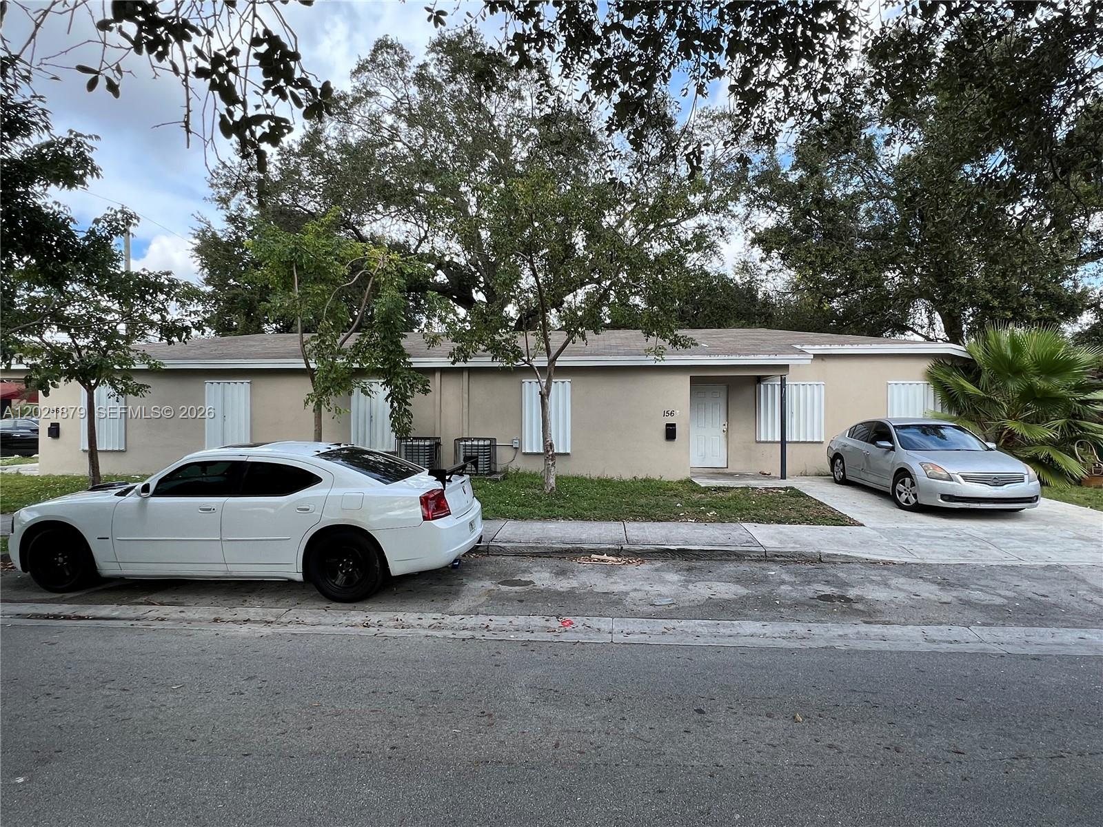 A single-story beige house with white hurricane shutters and two cars parked in front — 1565 NW 47th St, Miami FL 33142, MIAMI, FL