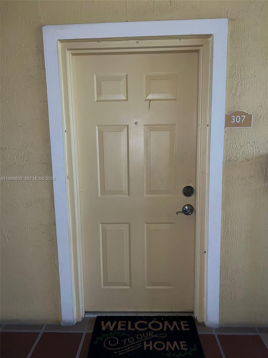 A beige six-panel entry door with a welcome mat is set in a stucco wall — 7220 NW 114th Ave # 307, Doral FL 33178, DORAL, FL