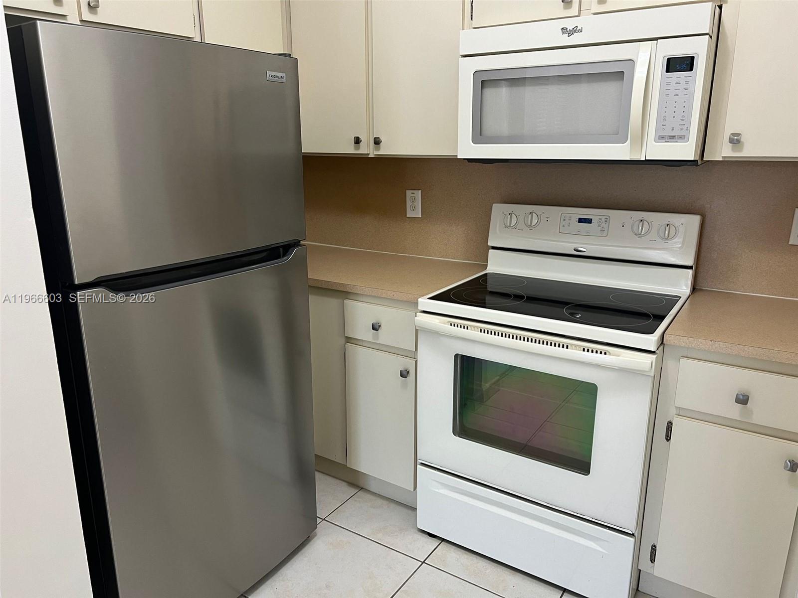 A kitchen features a stainless steel refrigerator, white appliances, and beige cabinets with countertops — 7220 NW 114th Ave # 307, Doral FL 33178, DORAL, FL