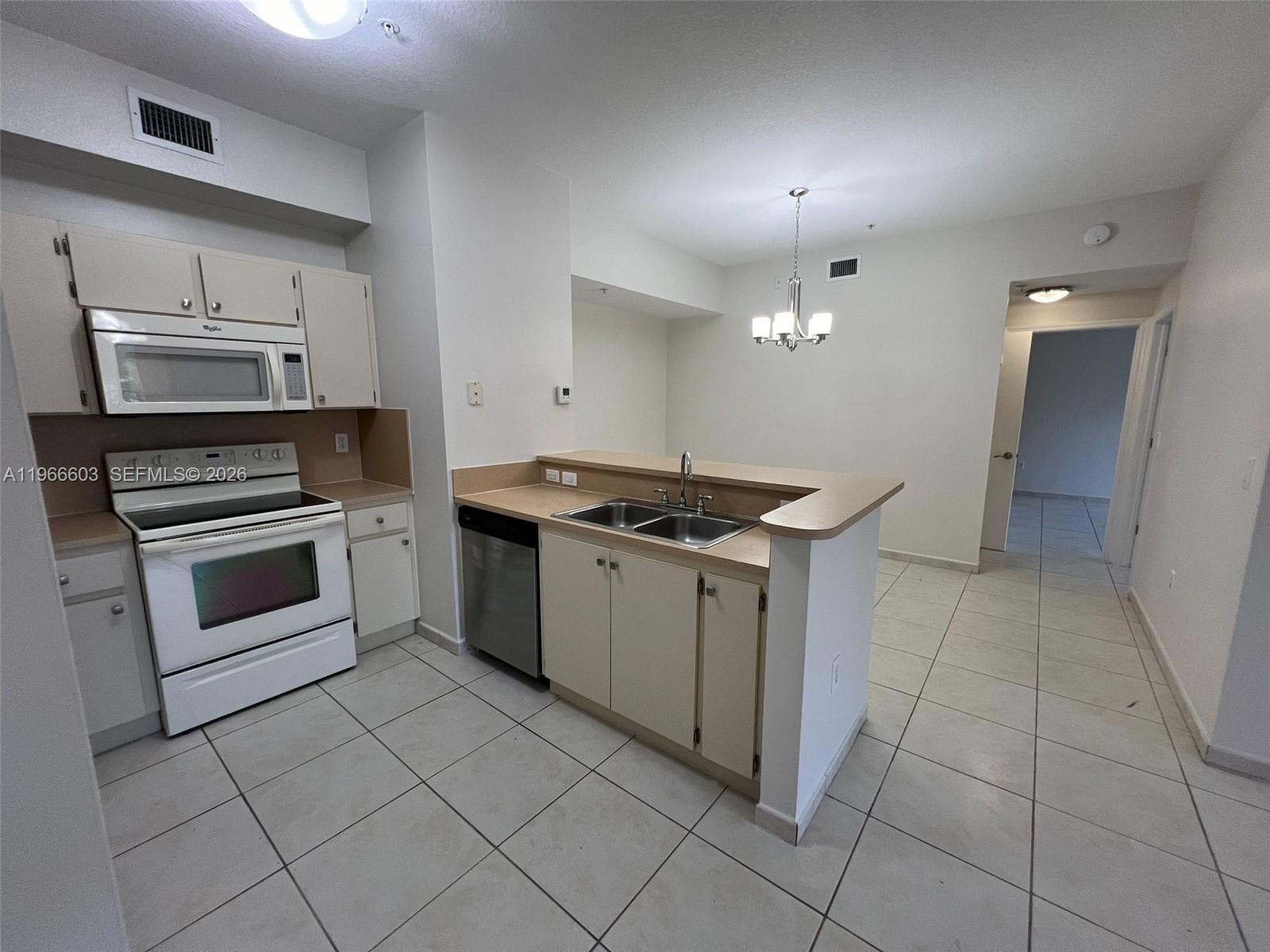 A kitchen features white appliances, light-colored cabinets, a peninsula sink, and tile flooring — 7220 NW 114th Ave # 307, Doral FL 33178, DORAL, FL