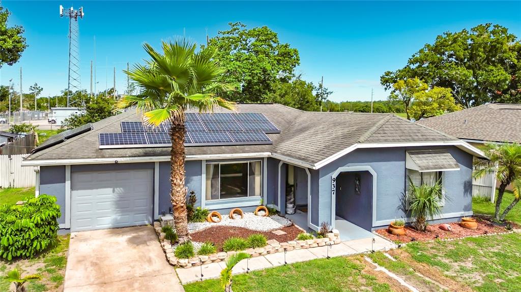 A blue single-story house features a solar panel array on the roof and a palm tree — 937 FLORIDA PARKWAY, KISSIMMEE, FL