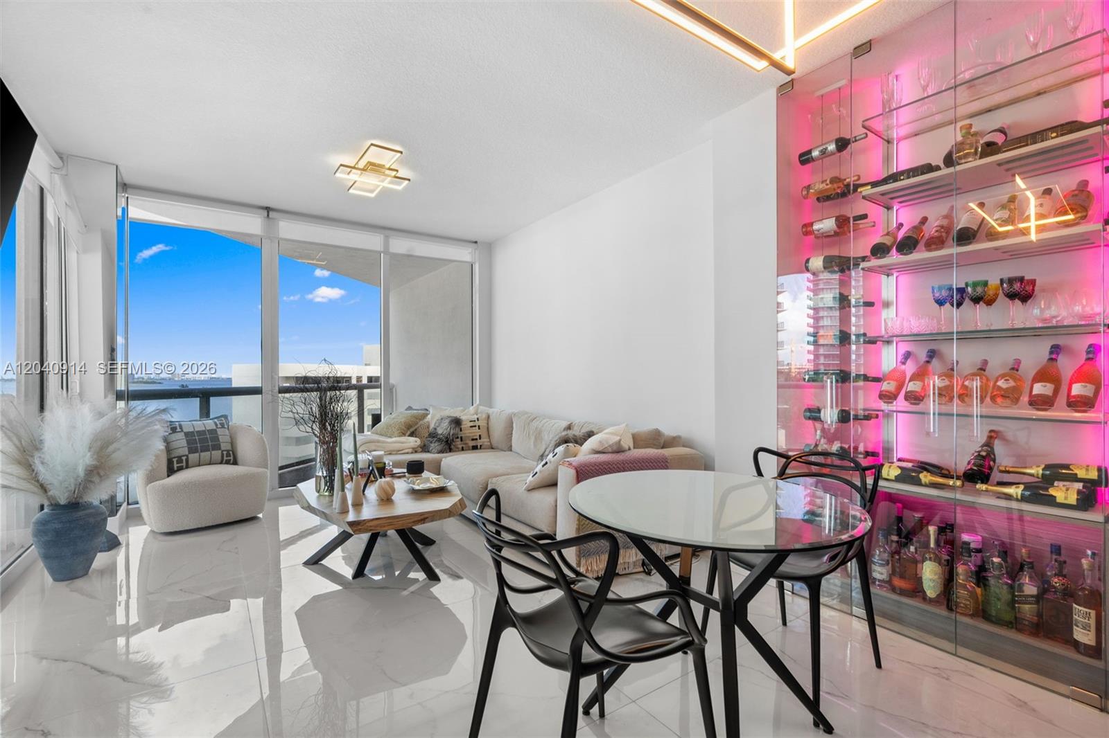 A living and dining area features a glass wine display, white tile floors, and balcony views — 480 NE 30th St # 904, Miami FL 33137, MIAMI, FL
