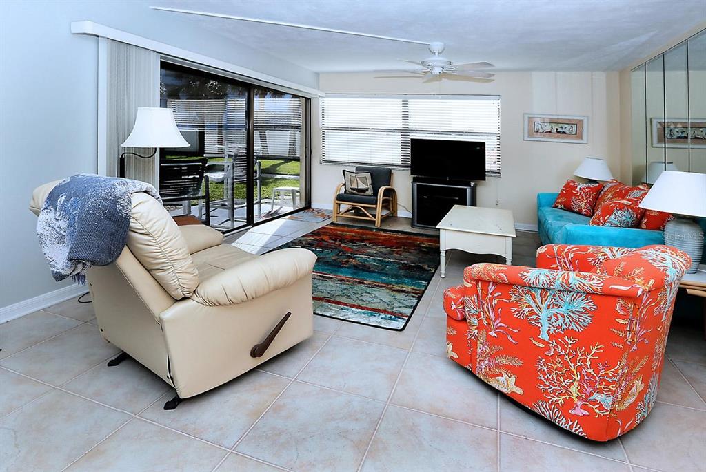 A living room features tile flooring, a colorful area rug, and a sliding glass door — 1571 S ATLANTIC AVENUE UNIT 103, NEW SMYRNA BEACH, FL