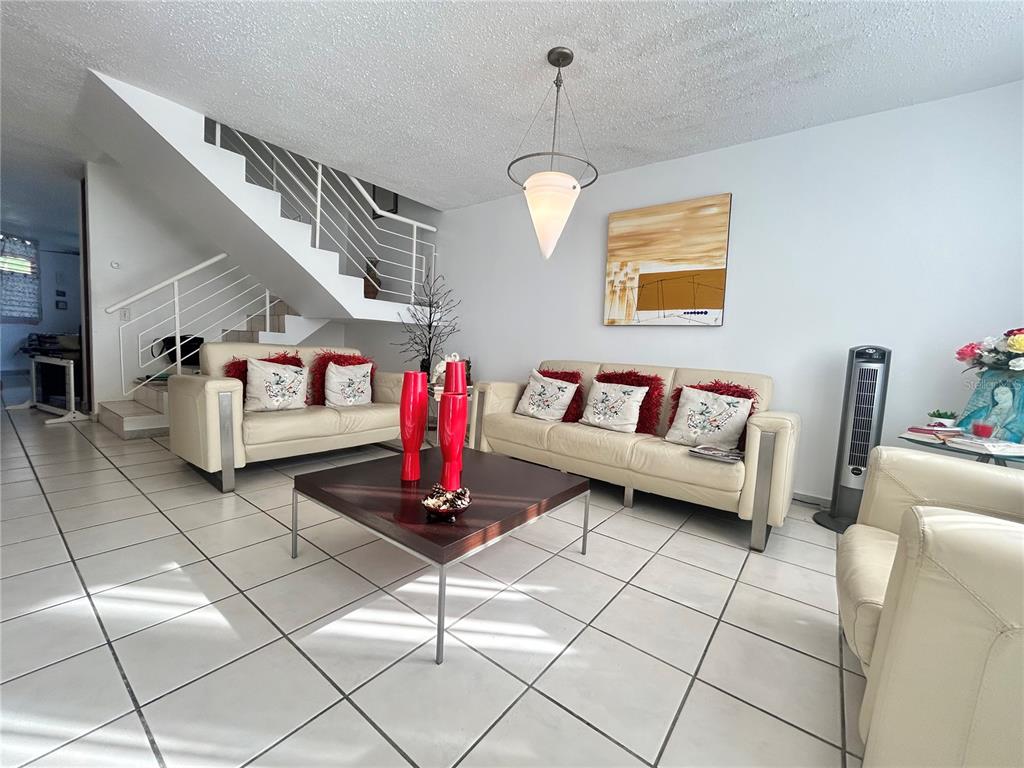 A living room features white tile floors, cream leather sofas, and a staircase with railings — PG-124 VIA ARCOIRIS, TRUJILLO ALTO, PR