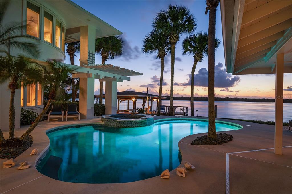A two-story house with a pool, patio, and palm trees at twilight — 1215 COMMODORE DRIVE, NEW SMYRNA BEACH, FL