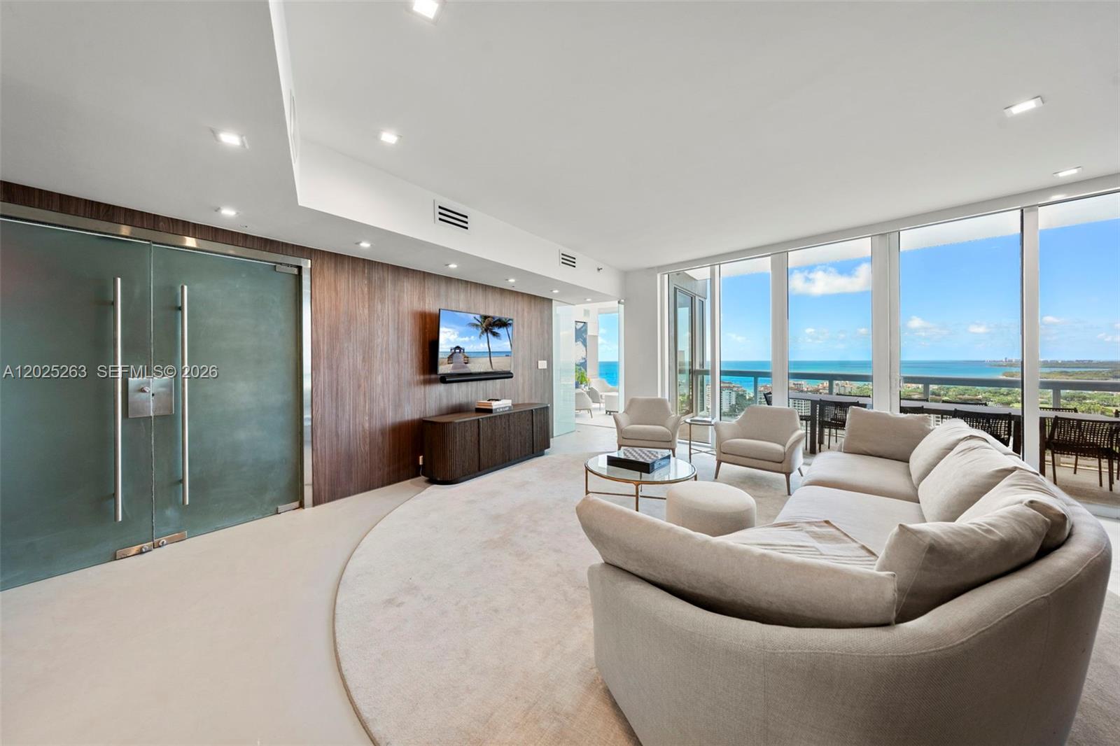 A modern living room features a curved rug, wood-paneled wall, and floor-to-ceiling ocean views — 1000 S Pointe Dr # 2803, Miami Beach FL 33139, MIAMI BEACH, FL