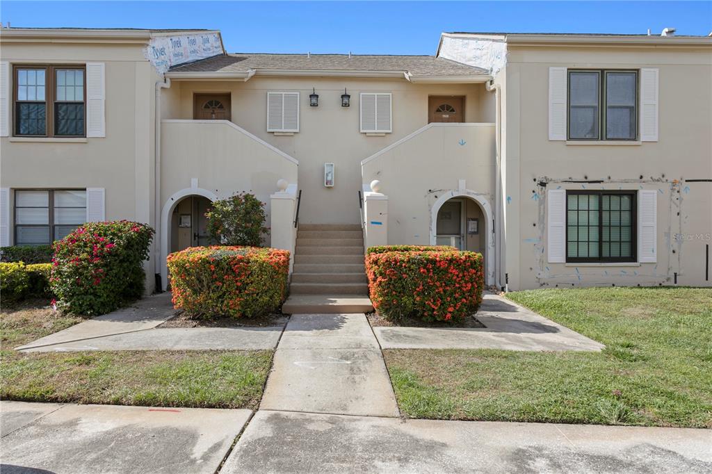 A two-story townhouse exterior features beige stucco walls, arched entryways, and a central staircase — 2453 KINGFISHER LANE UNIT G202, CLEARWATER, FL