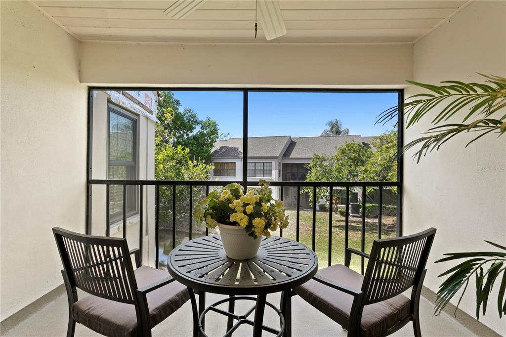 A screened-in balcony features a small round table with yellow flowers and two chairs — 2453 KINGFISHER LANE UNIT G202, CLEARWATER, FL