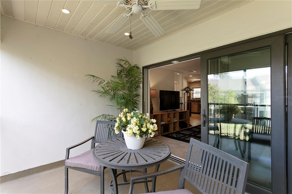 A covered patio features a small round table, two chairs, a potted plant, and sliding doors — 2453 KINGFISHER LANE UNIT G202, CLEARWATER, FL