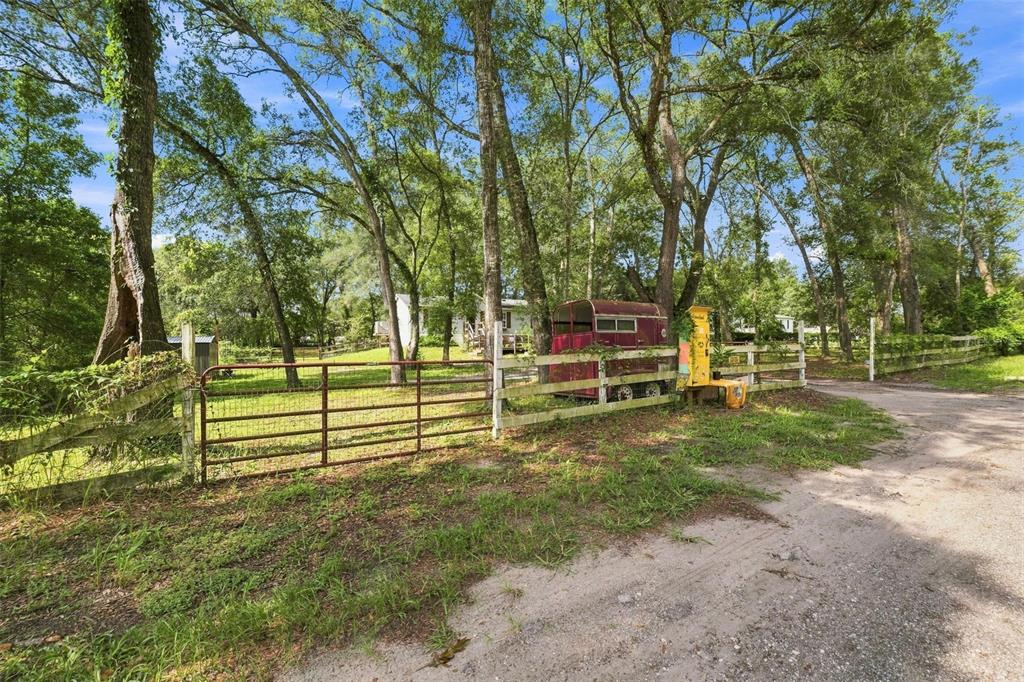 A dirt driveway leads to a gated entrance with a red horse trailer and trees — 18051 PORSCHE PLACE, SPRING HILL, FL