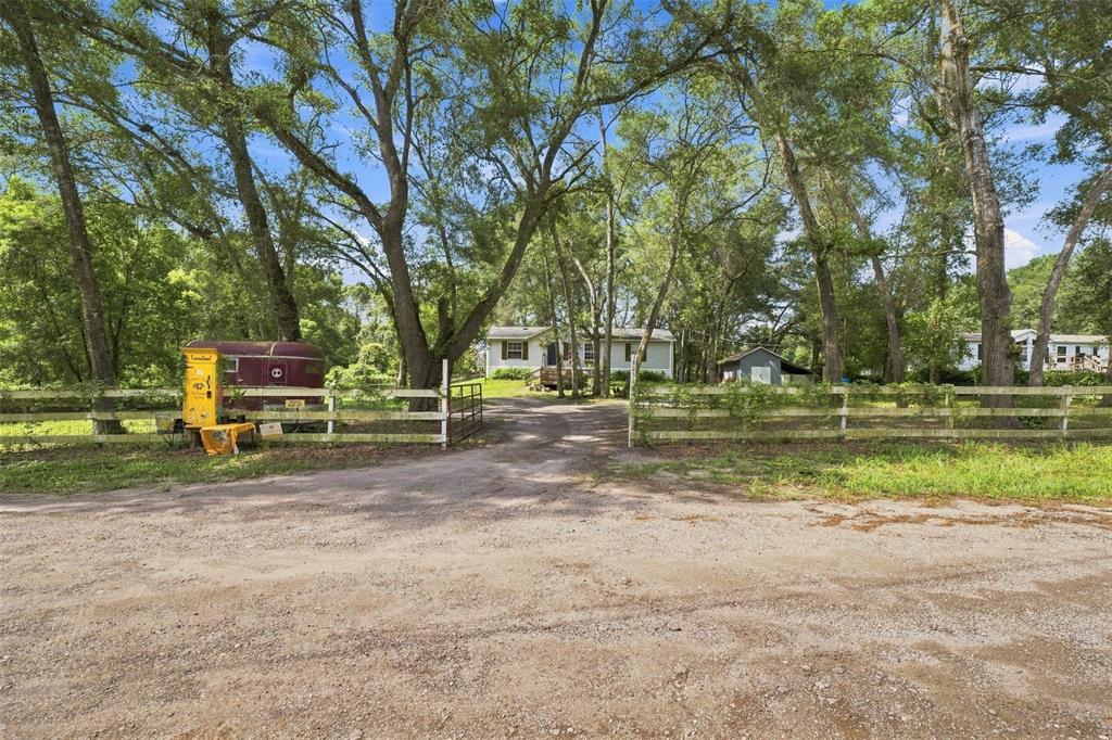 A gravel driveway leads through a white fence to a house surrounded by many trees — 18051 PORSCHE PLACE, SPRING HILL, FL