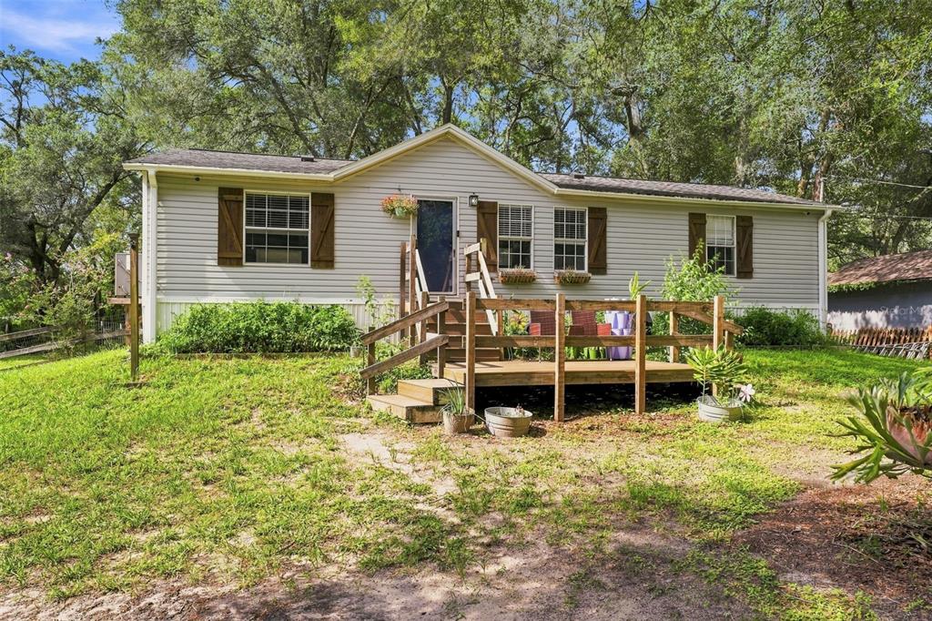 A single-story house with light gray siding, brown shutters, and a wooden front deck — 18051 PORSCHE PLACE, SPRING HILL, FL