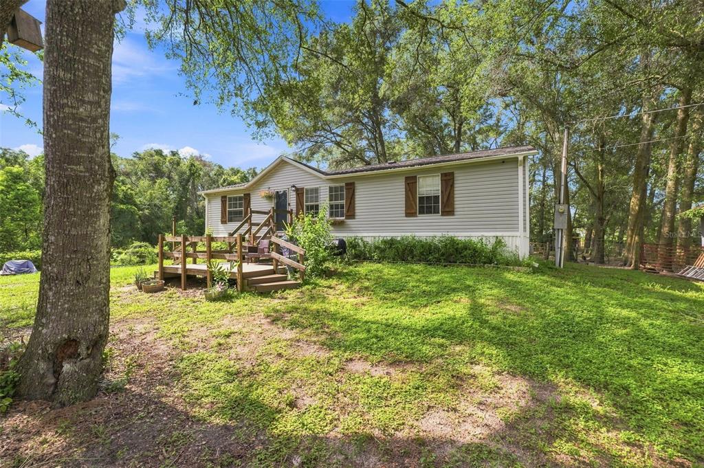 A single-story house with light gray siding and a wooden deck sits on a grassy lot — 18051 PORSCHE PLACE, SPRING HILL, FL