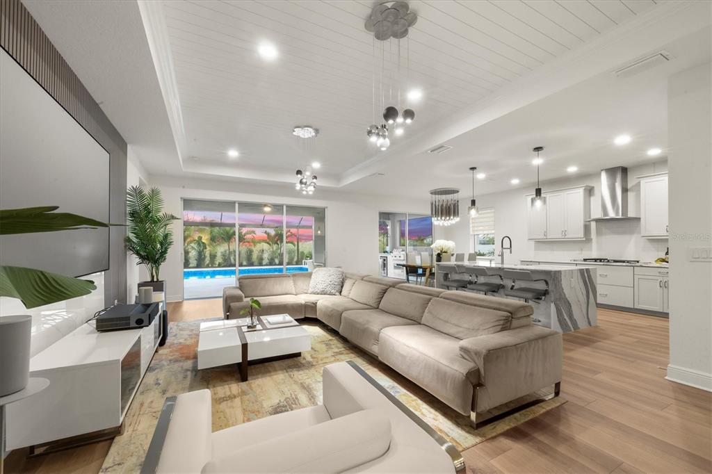An open-concept living room and kitchen featuring a large sectional sofa and pool view — 17727 SAVORY MIST CIRCLE, BRADENTON, FL