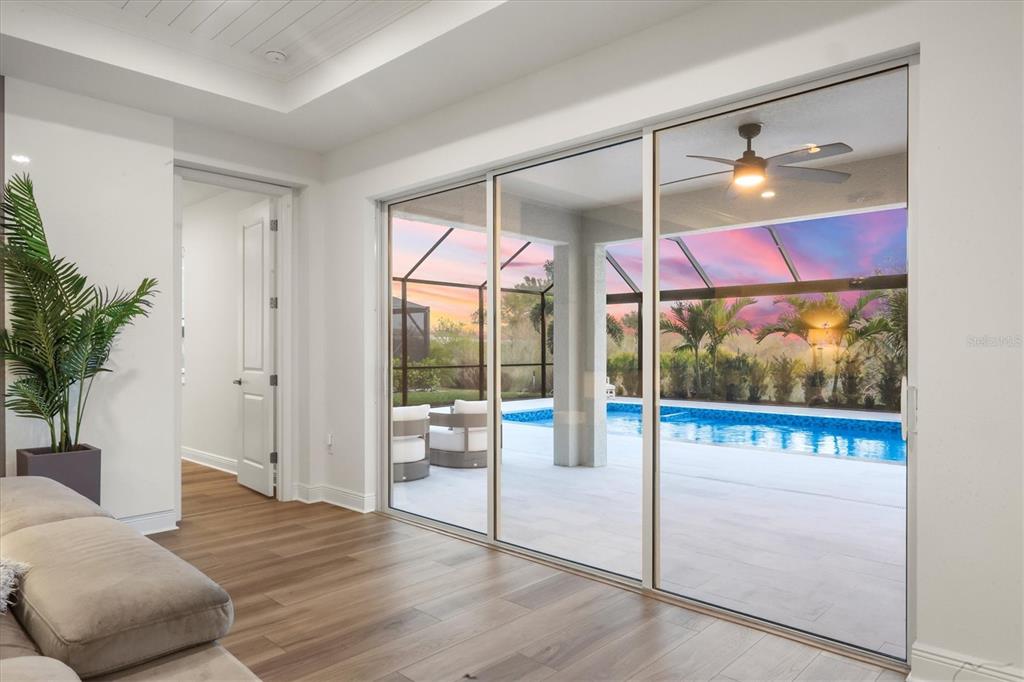 A living room with wood floors features large sliding glass doors overlooking a pool deck — 17727 SAVORY MIST CIRCLE, BRADENTON, FL