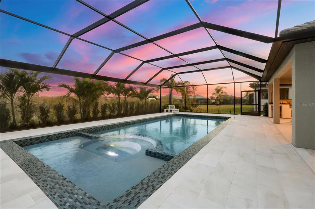 A swimming pool with a built-in spa sits inside a screened lanai at sunset — 17727 SAVORY MIST CIRCLE, BRADENTON, FL
