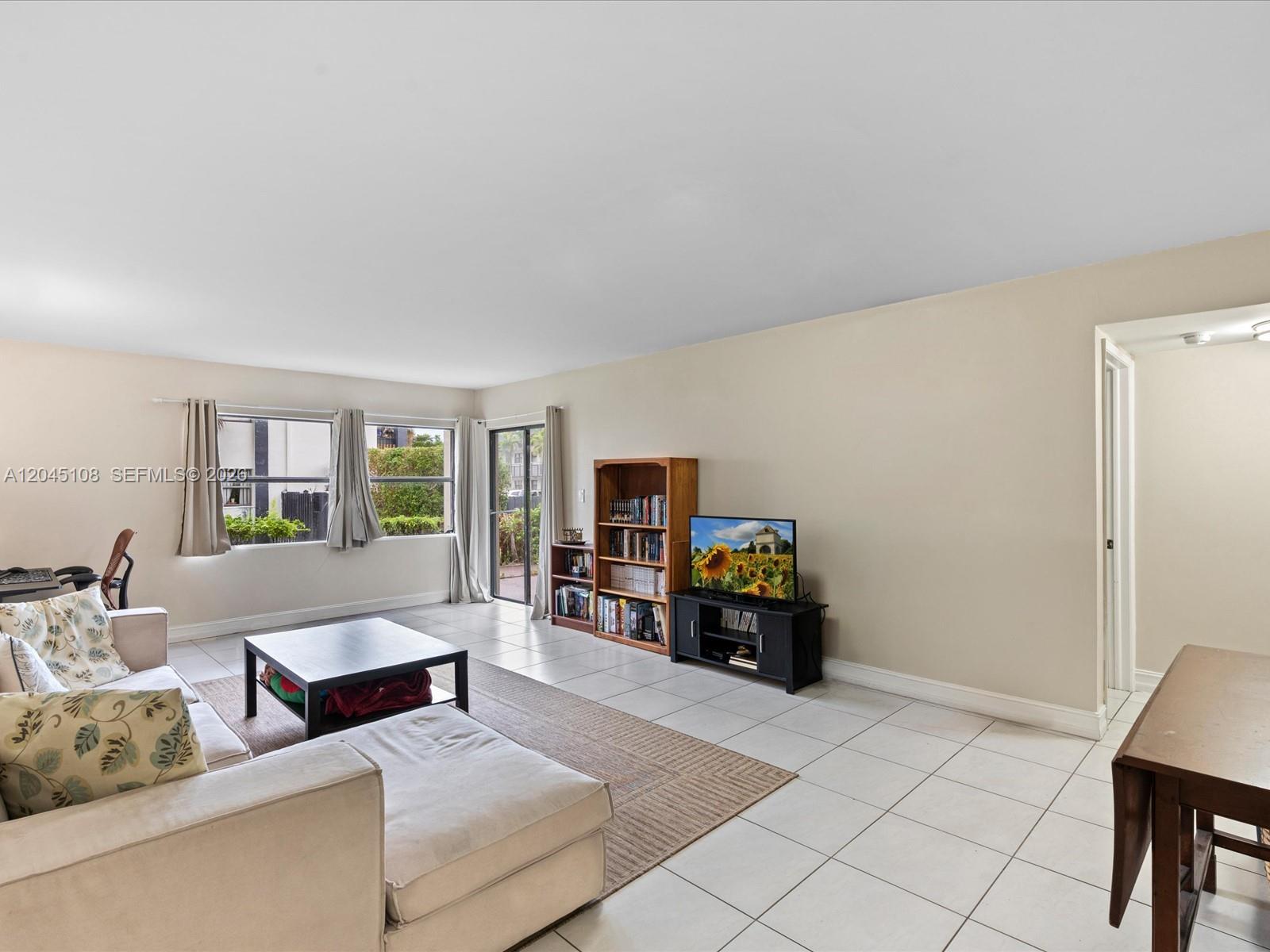 A living room features a sectional sofa, a coffee table, a bookshelf, and tile flooring — 571 NW 107th Ave # 107, Miami FL 33172, MIAMI, FL