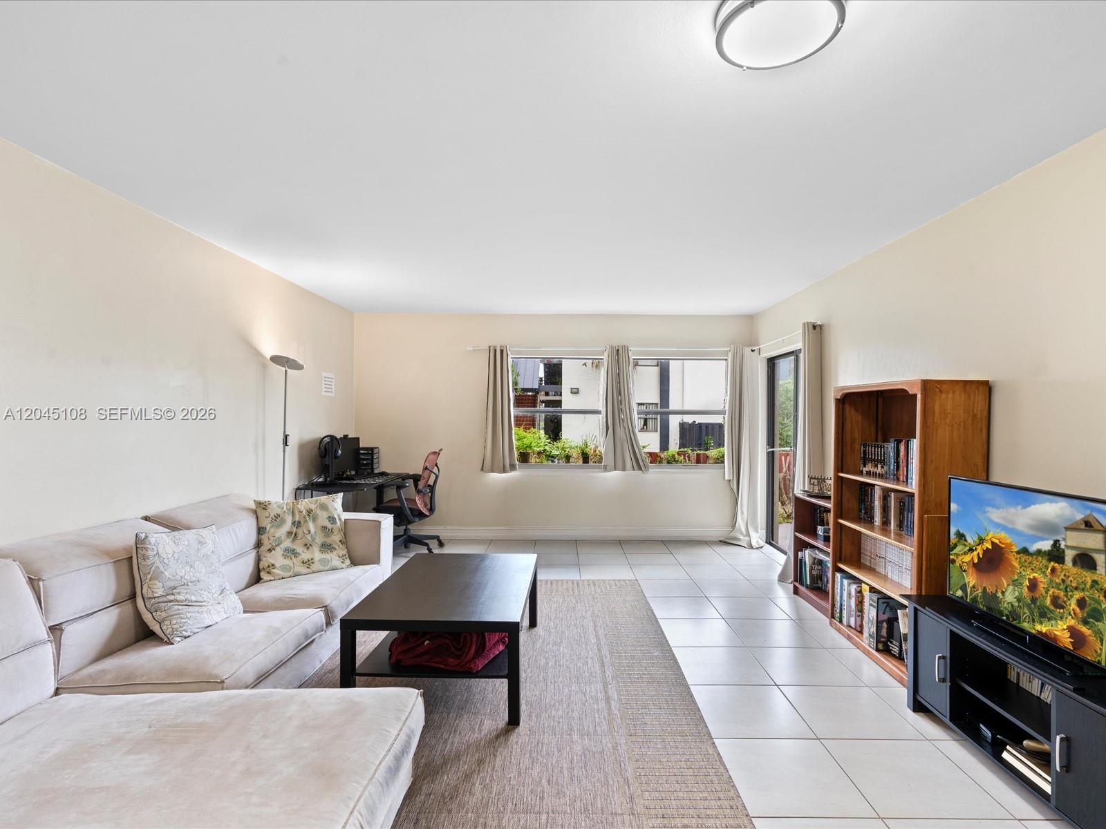 A living room features light-colored tile floors, a sectional sofa, a desk, and a bookshelf — 571 NW 107th Ave # 107, Miami FL 33172, MIAMI, FL