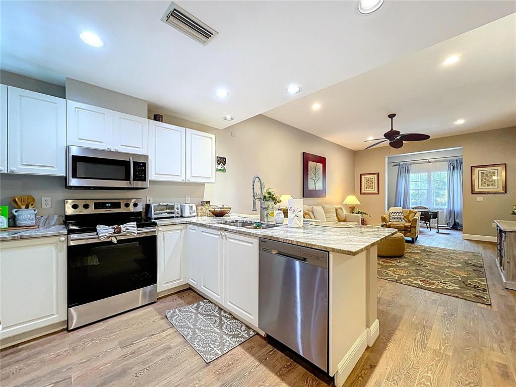 A kitchen with white cabinets and stainless steel appliances opens into a living area — 3803 54TH DRIVE W UNIT 102, BRADENTON, FL