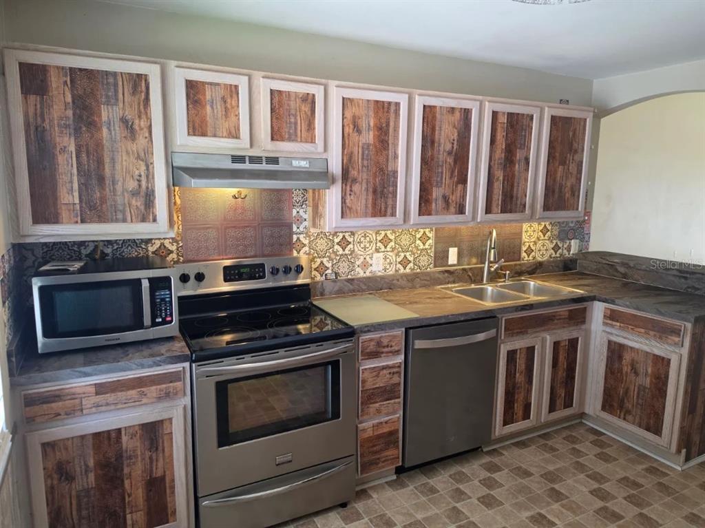 A kitchen features wood-look cabinet panels, patterned tile backsplashes, and stainless steel appliances — 416 EAGLE RIDGE DRIVE UNIT 416, DAVENPORT, FL