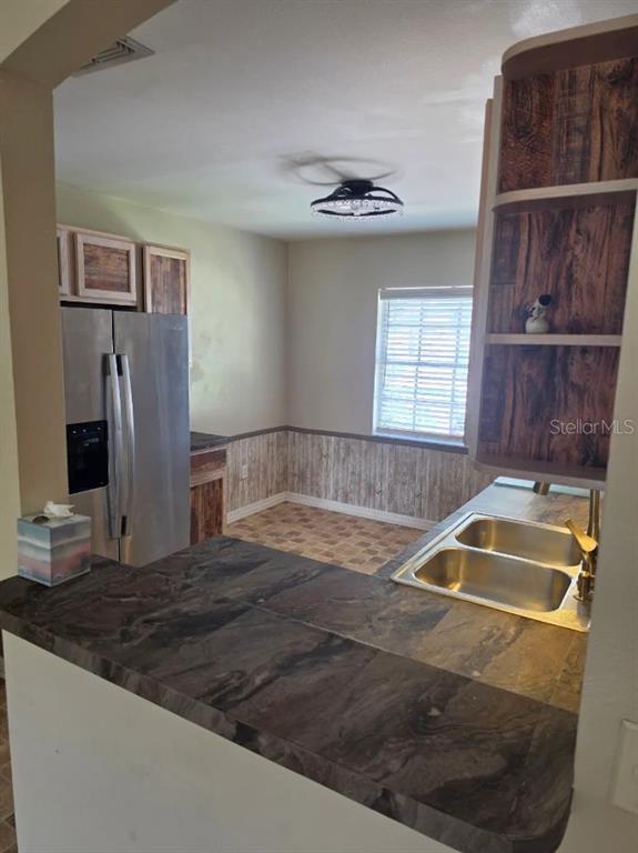 A kitchen features a dark stone countertop, stainless steel refrigerator, and wood-patterned cabinetry — 416 EAGLE RIDGE DRIVE UNIT 416, DAVENPORT, FL