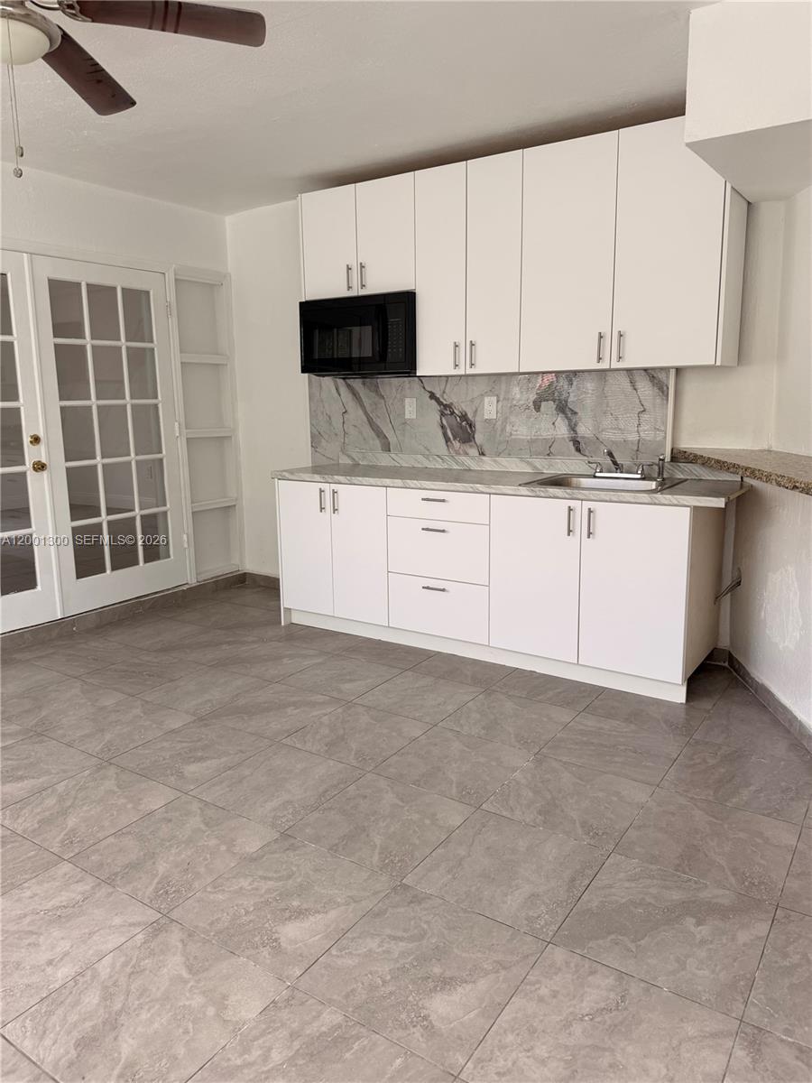 A kitchen features white cabinets, a marble-patterned backsplash, and gray tile flooring — 6613 Evergreen Dr # B, Miramar FL 33023, MIRAMAR, FL