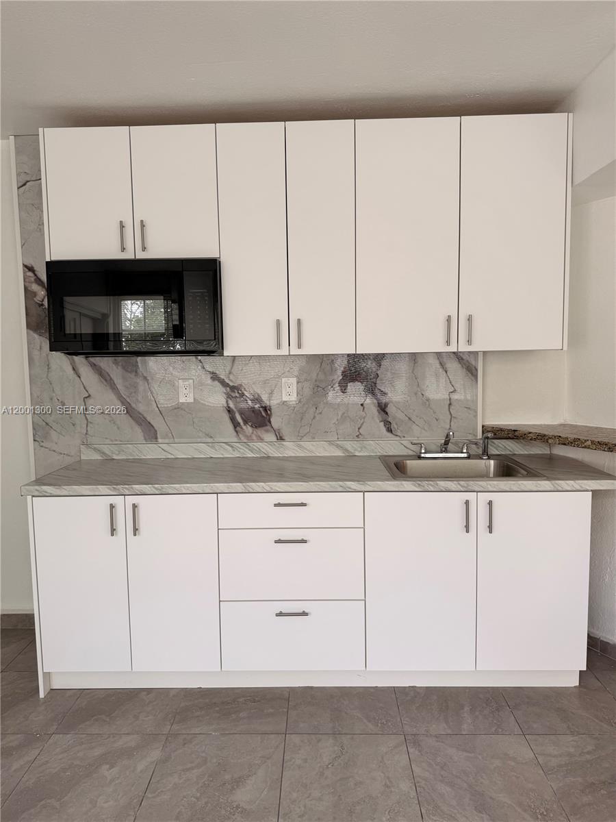 A kitchen features white cabinets, a black microwave, and a marble-patterned backsplash and countertop — 6613 Evergreen Dr # B, Miramar FL 33023, MIRAMAR, FL
