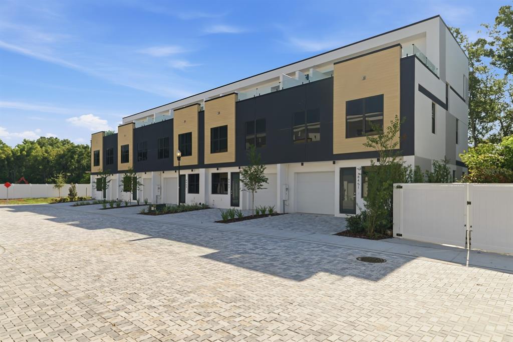A row of modern three-story townhomes with garages and light-colored brick paving in front — 8458 MODANO PLACE, TAMPA, FL