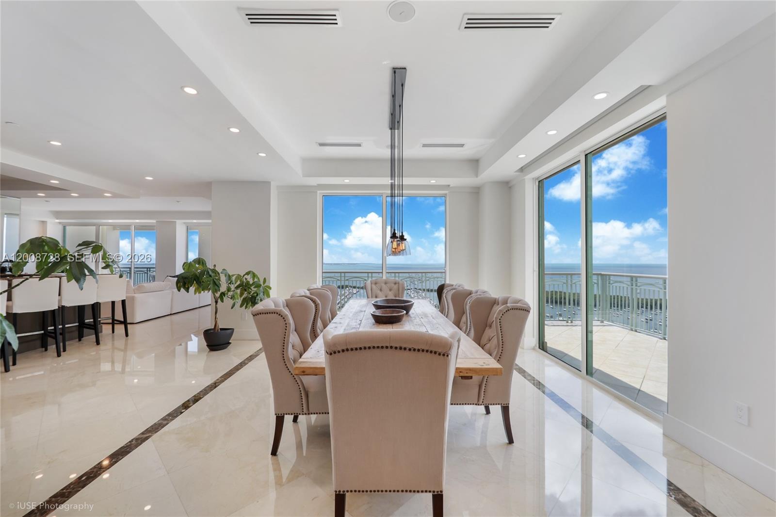 A dining room features a long wooden table, tufted chairs, and floor-to-ceiling ocean views — 3400 SW 27th Ave # 2202, Miami FL 33133, MIAMI, FL