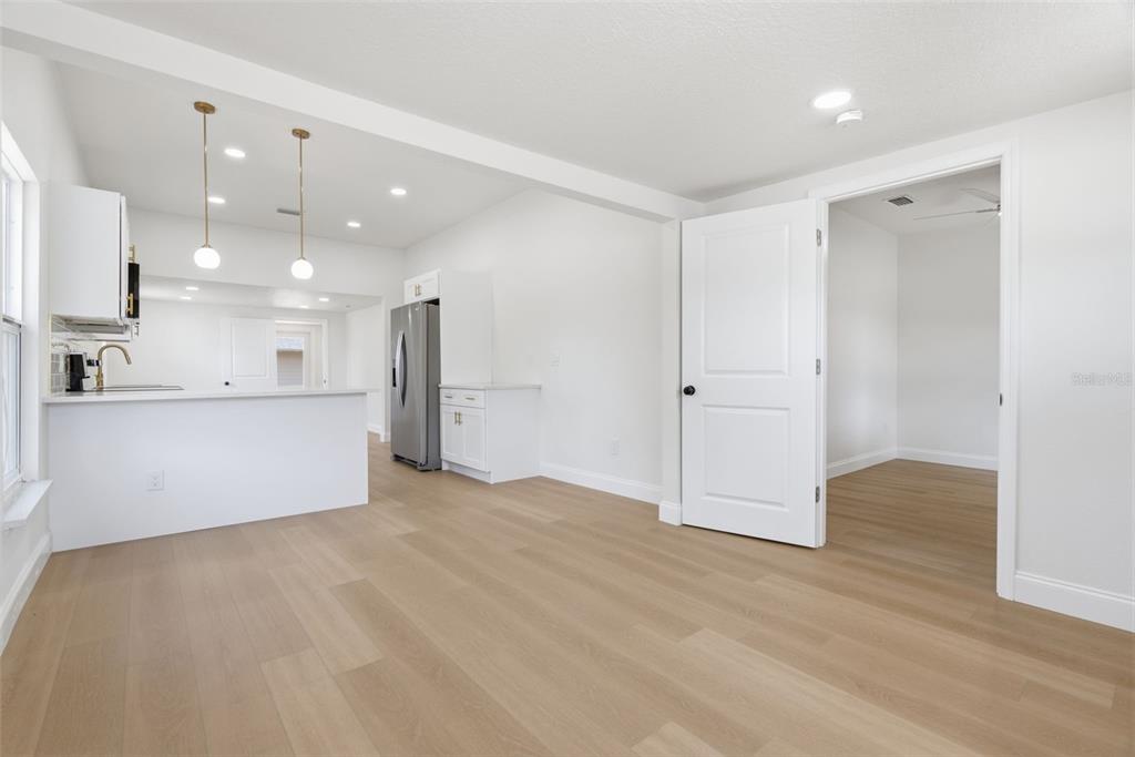 A bright, open-concept kitchen and dining area features white cabinetry, stainless appliances, and light wood flooring — 1700 SCRANTON STREET S, ST PETERSBURG, FL